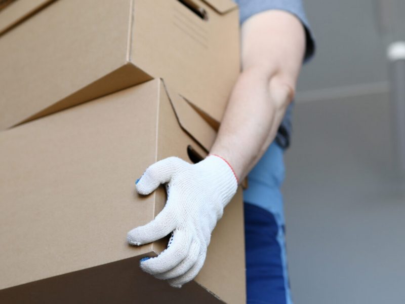 Man in work clothes and gloves carries cardboard boxes. Folding boxes. Moving waiting for loading service. Things are collected for moving. Collection goods in warehouse online store during quarantine